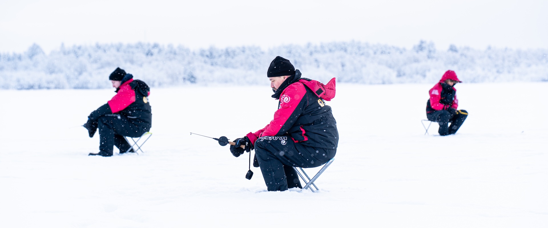 People in winter suits ice fishing on the frozen Baltic Sea during the Catch a Fish workshop, snow falling. Photo: Vera Lakovaara