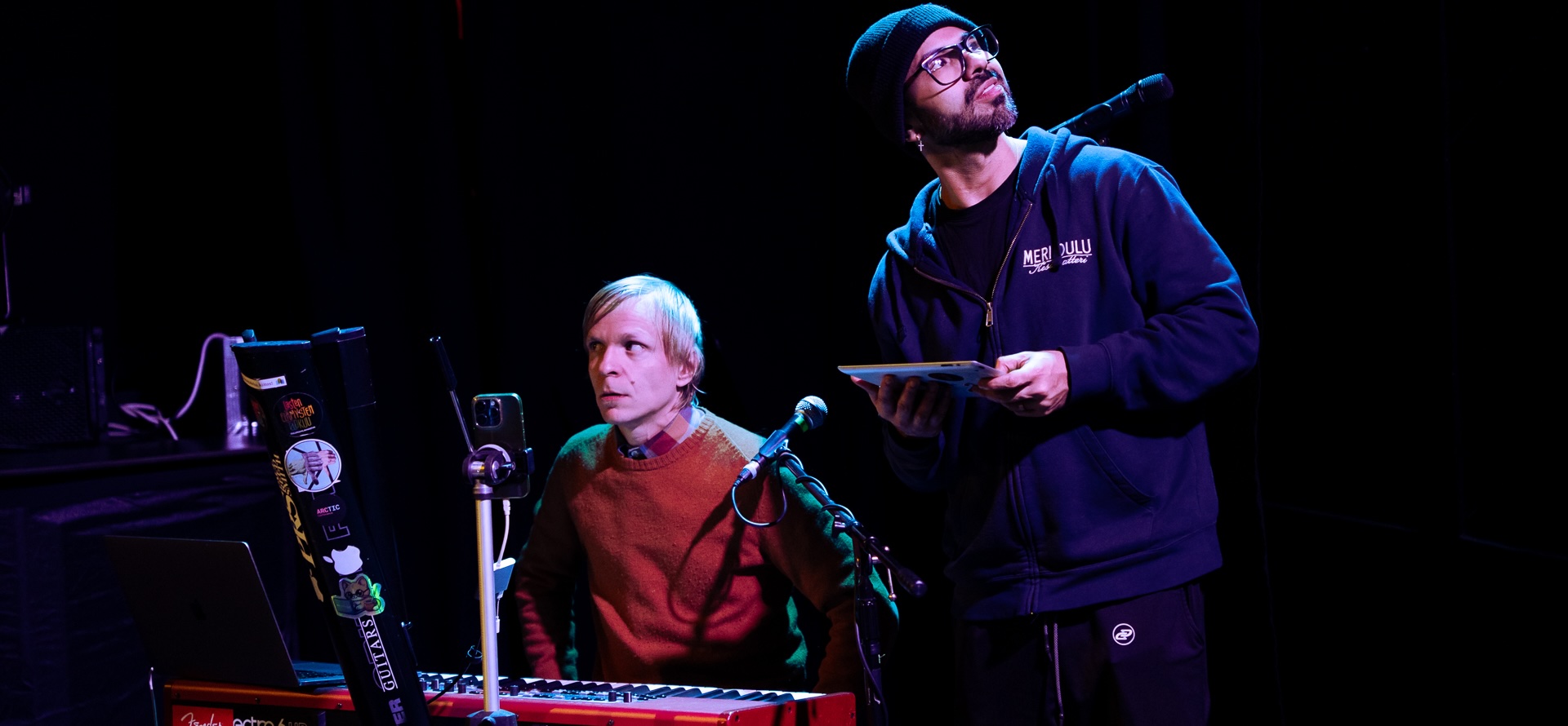 A musician at a keyboard and a technician holding a tablet at a microphone on a blue-lit stage. Photo: Vera Lakovaara