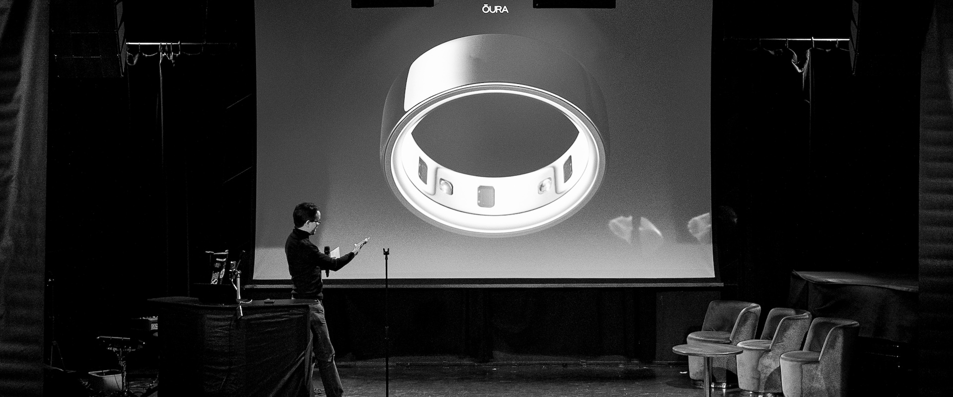 Janne Käki of Oura, the conference's main sponsor, presenting on a dark stage in front of a giant projected photo of an Oura smart ring. Photo: Vera Lakovaara